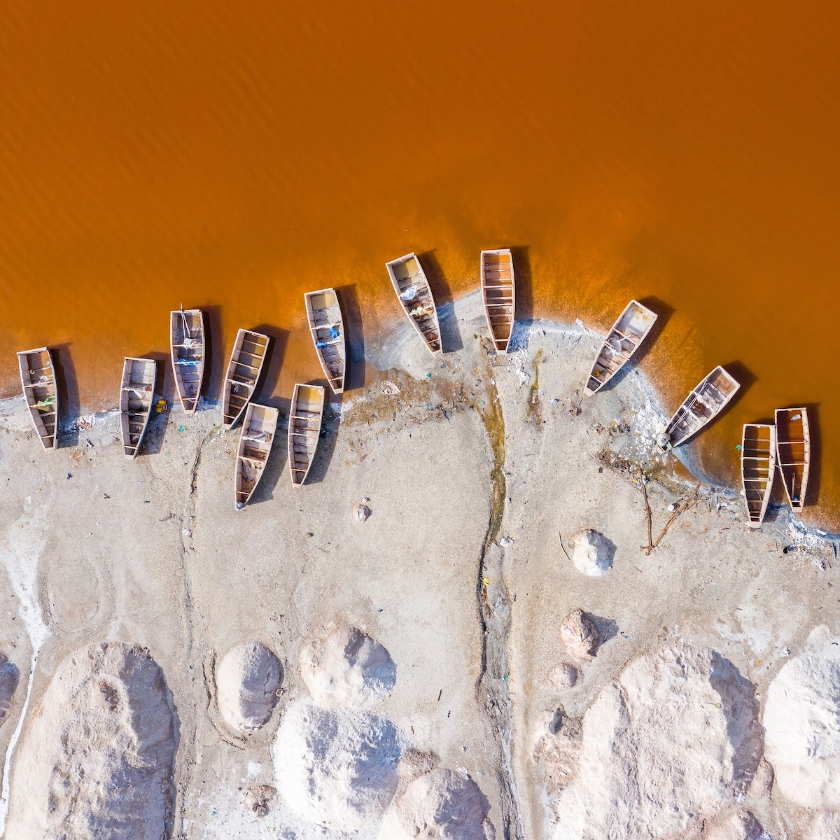 Several wooden boats laying on shore at an orange brown lake